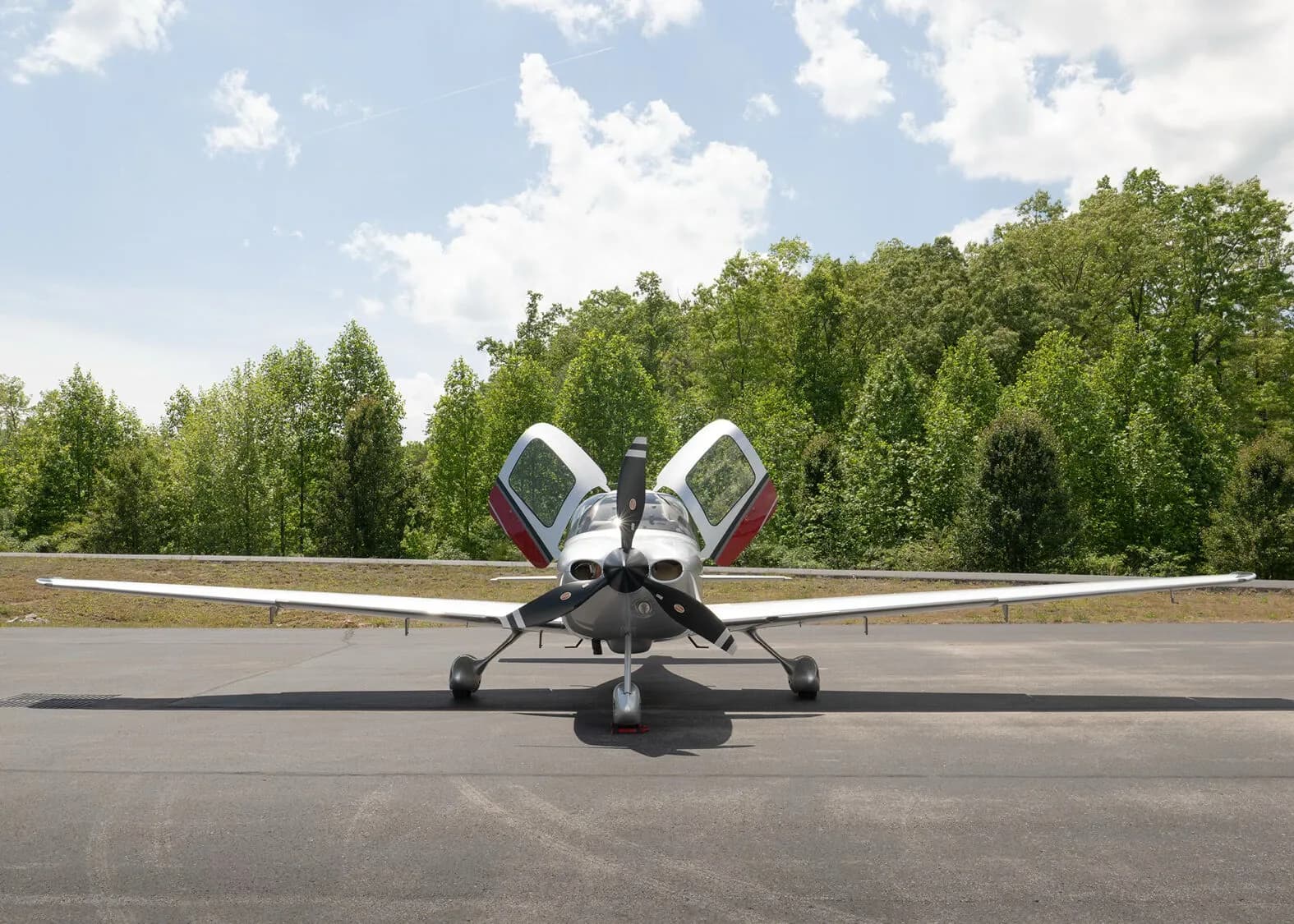 A front view of a silver and red Cirrus SR22 aircraft, N224KR, with its gull-wing doors open, parked on an asphalt ramp.