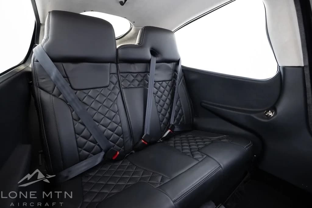 The black leather rear seats of an aircraft cabin with diamond stitching.