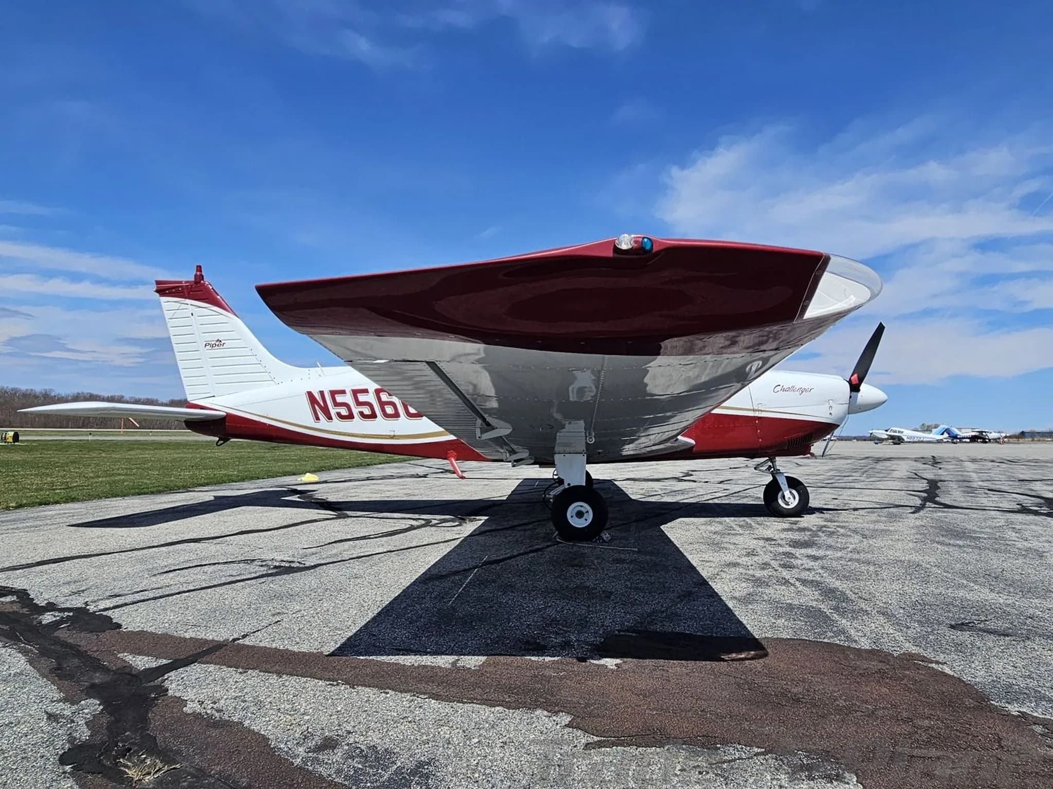 Side view of a white and maroon Piper PA-28 Challenger aircraft with registration N55667 parked on an airfield.