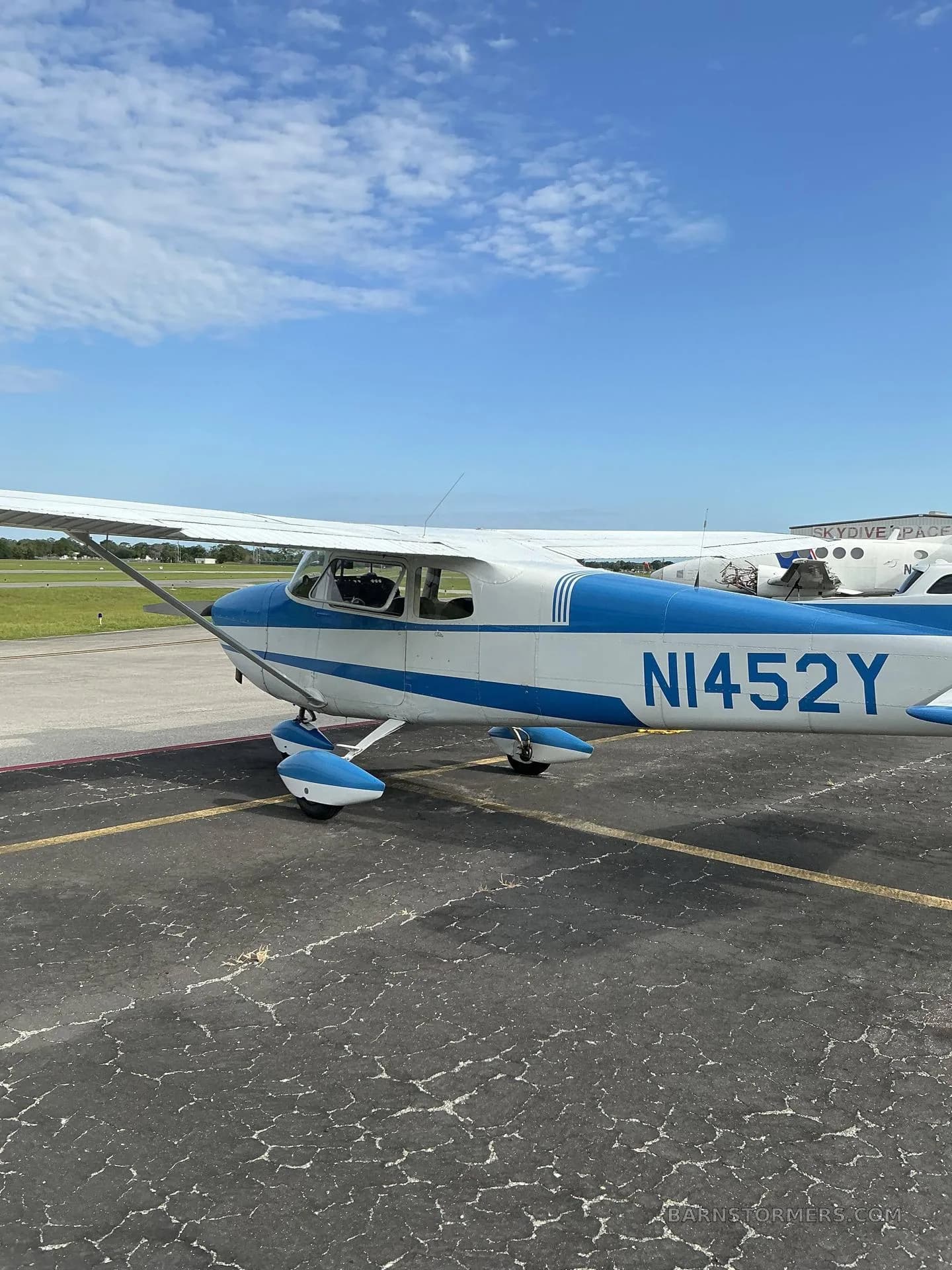 A white and blue Cessna 172 aircraft with tail number N1452Y is parked on an asphalt ramp, viewed from the right side.
