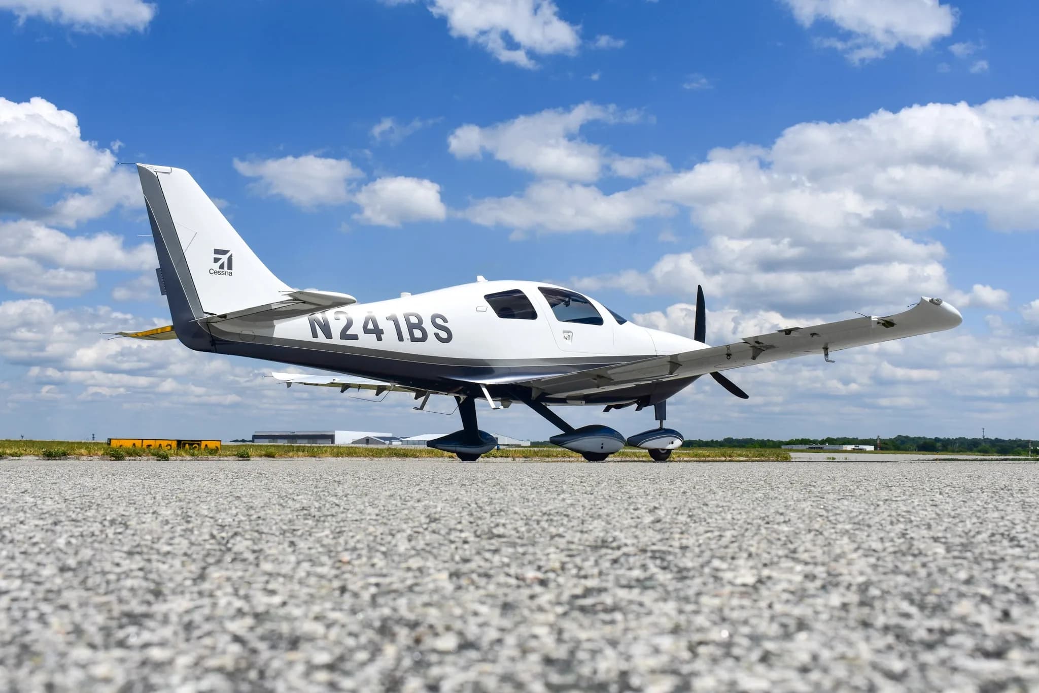 A low-angle side view of a white and dark grey Cessna TTx (Corvalis 400) aircraft, N241BS, parked on an airfield.