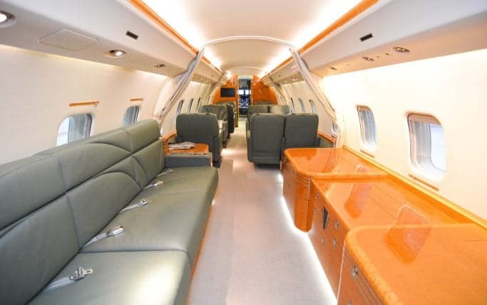 View of the aircraft's interior cabin with leather seats, tables, and wood trim.