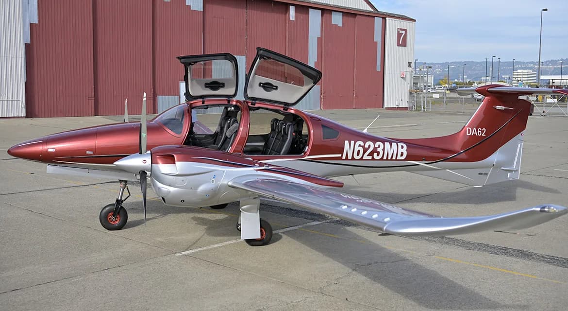 A maroon and silver Diamond DA62 aircraft is parked on the tarmac with its doors open.