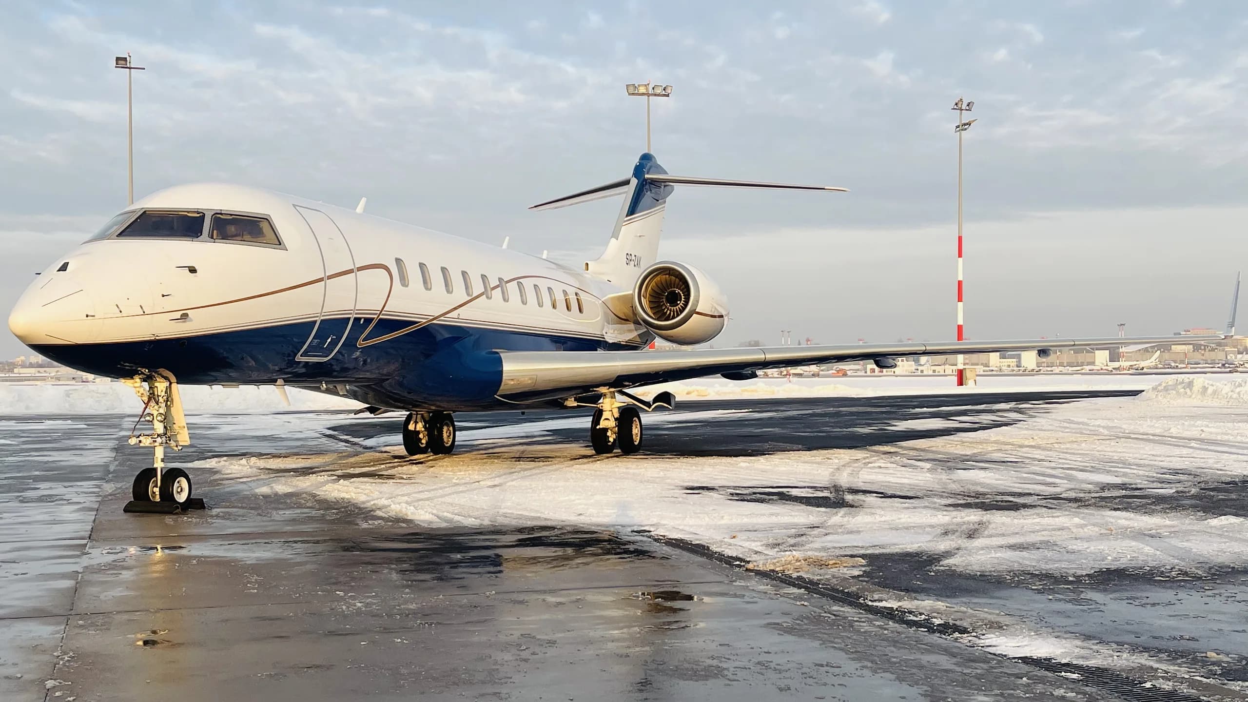A white and blue private jet parked on a snow-covered tarmac on a clear winter day.