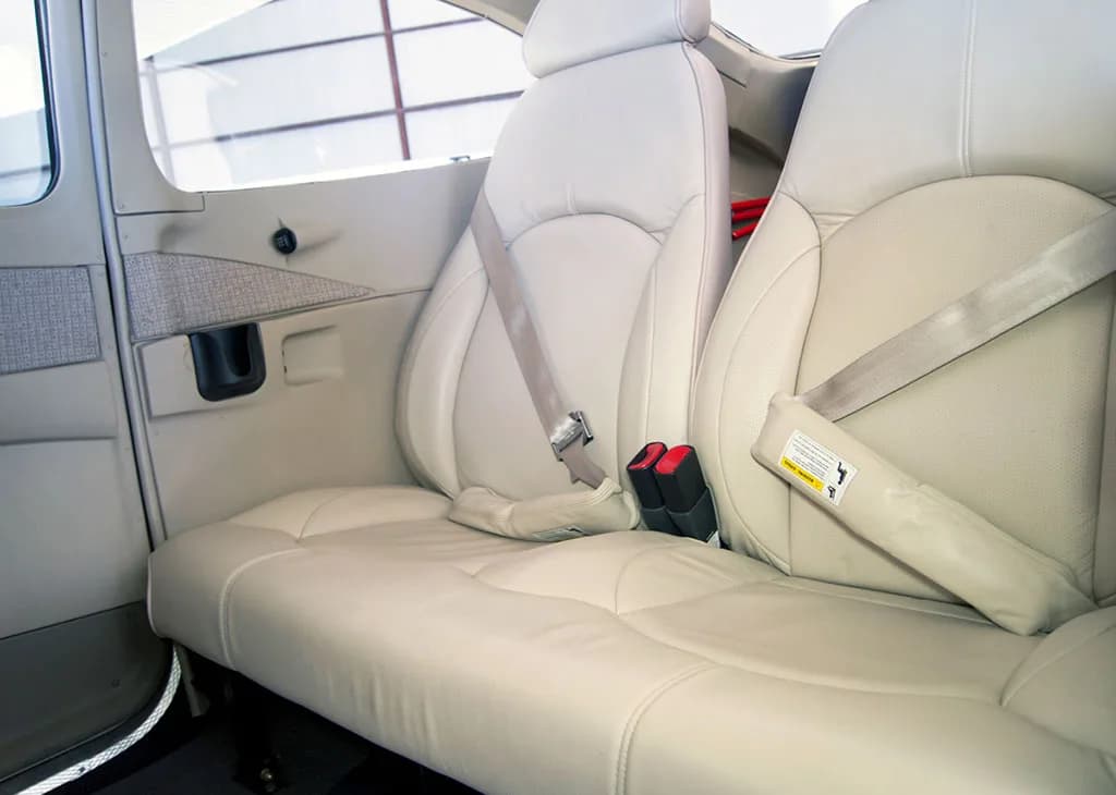 The light beige leather passenger seats and rear bench seat of an aircraft cabin.