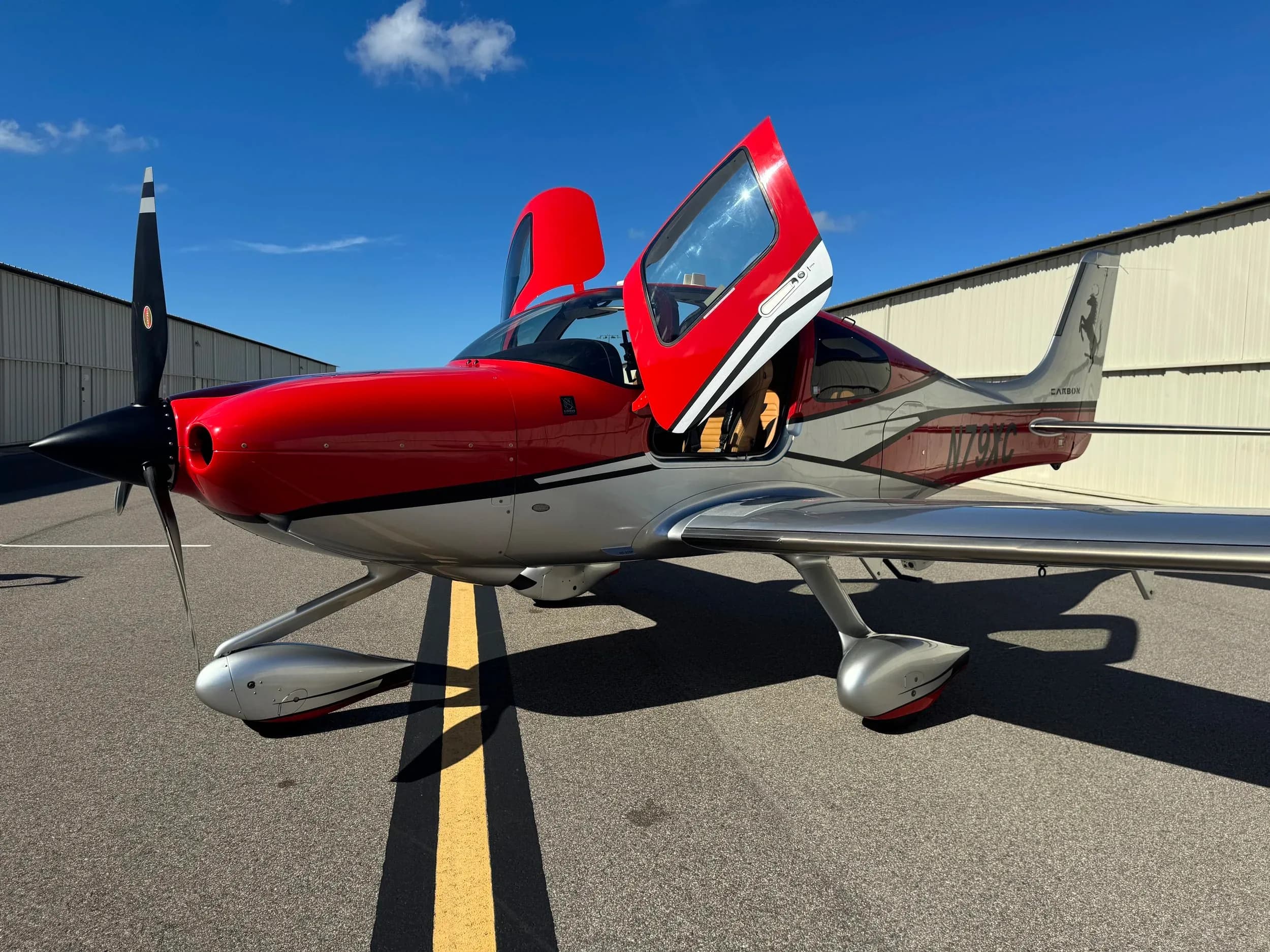 A Cirrus SR22T with a red and silver paint scheme has its doors open on the tarmac.
