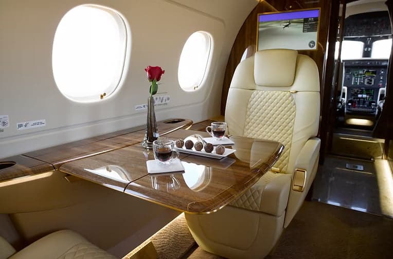A view of the interior of the aircraft with cream-colored leather seats and a wooden table.