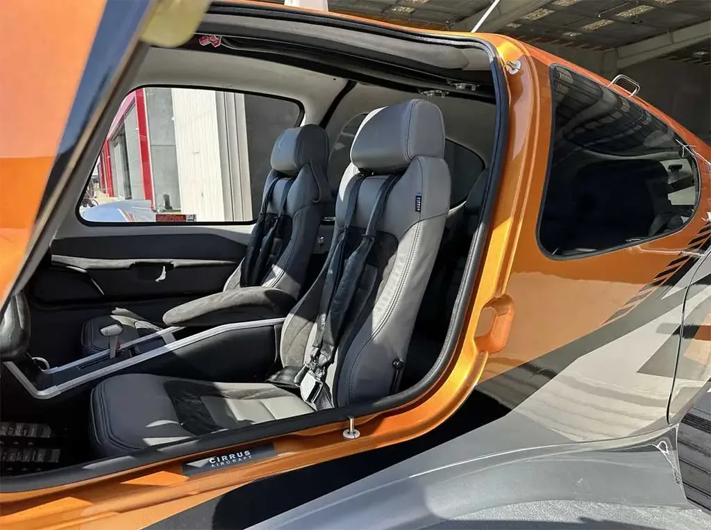 The interior of an orange and silver Cirrus SR22 aircraft, showing the grey leather seats and cabin.