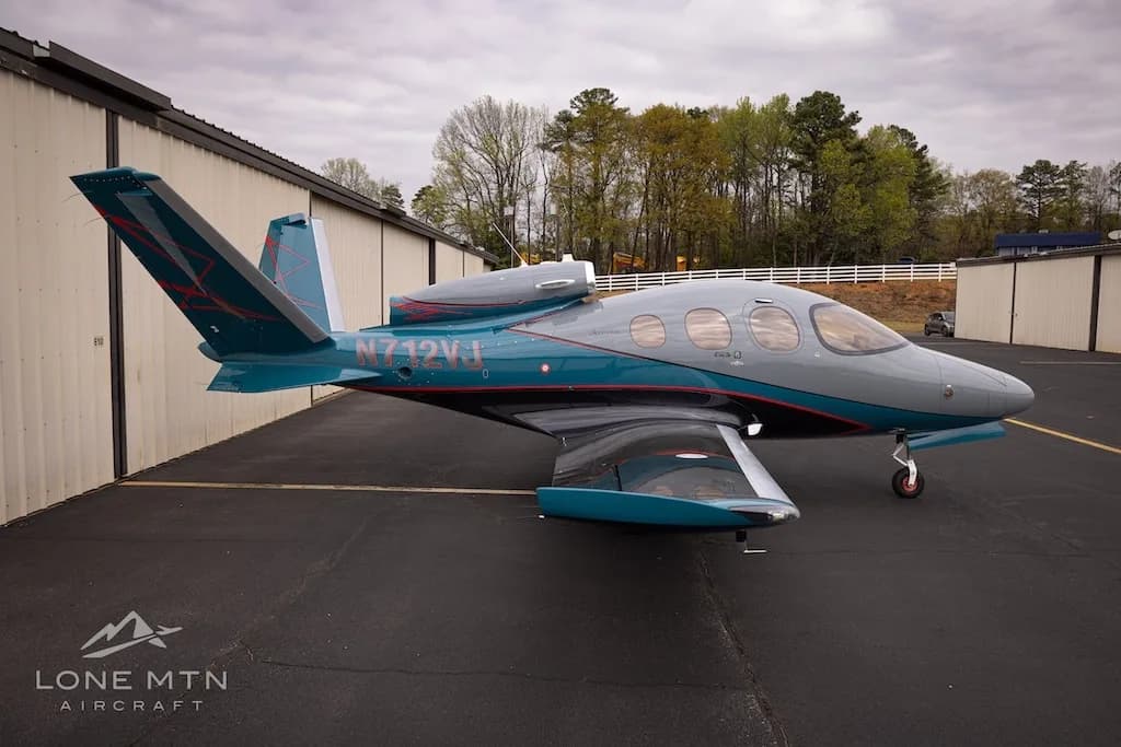 A side view of the Cirrus Vision Jet (N712VJ) with grey and teal livery, parked on an airfield.