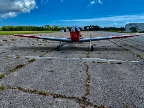 Front view of a red and white aircraft on a cracked concrete runway.