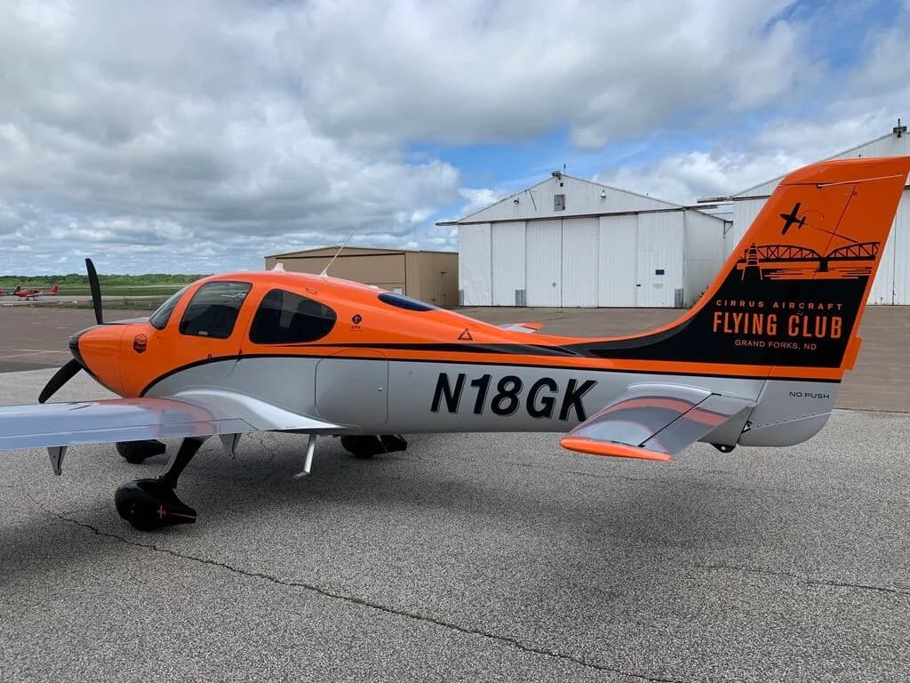 Side view of a Cirrus SR20 aircraft with orange, black, and silver paint scheme, showing the N18GK registration and tail logo.