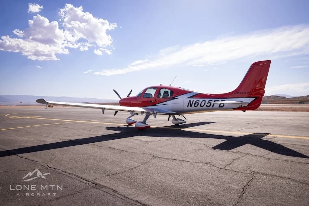 A rear-quarter view of a red and silver Cirrus SR22T aircraft (N605FB) with its tail facing the viewer, on an airfield.