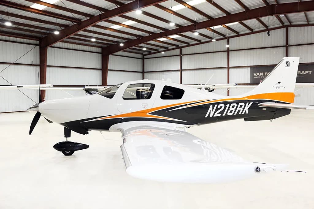 Side view of a white, black, and orange Cessna TTX aircraft with registration N218RK, inside a hangar.