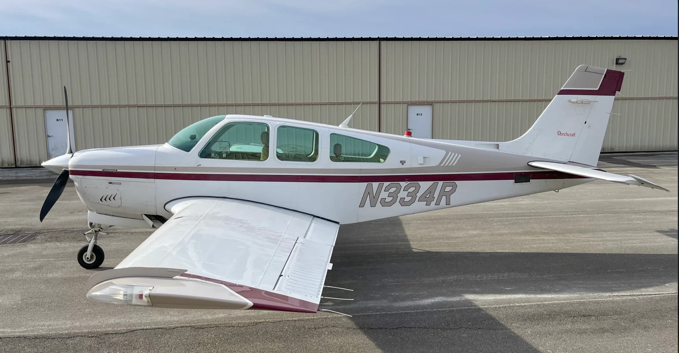 A side view of a white and maroon Beechcraft Bonanza aircraft, tail number N334R, parked on a tarmac.