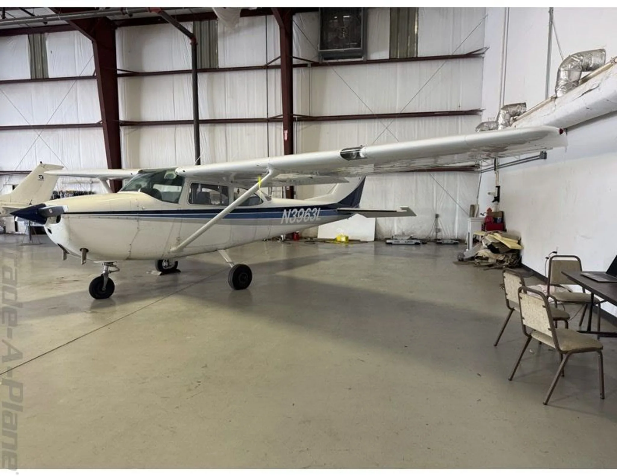 A white Cessna 172 with blue and grey stripes, registration N3963L, parked in a hangar.
