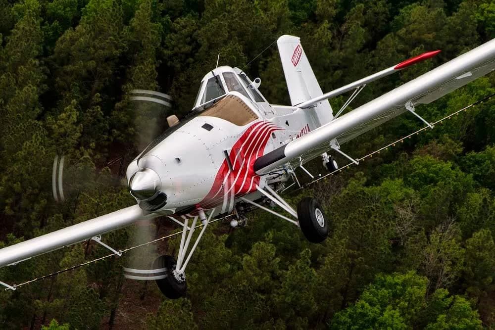 Air Tractor crop duster flying low over trees with a red and white paint scheme.