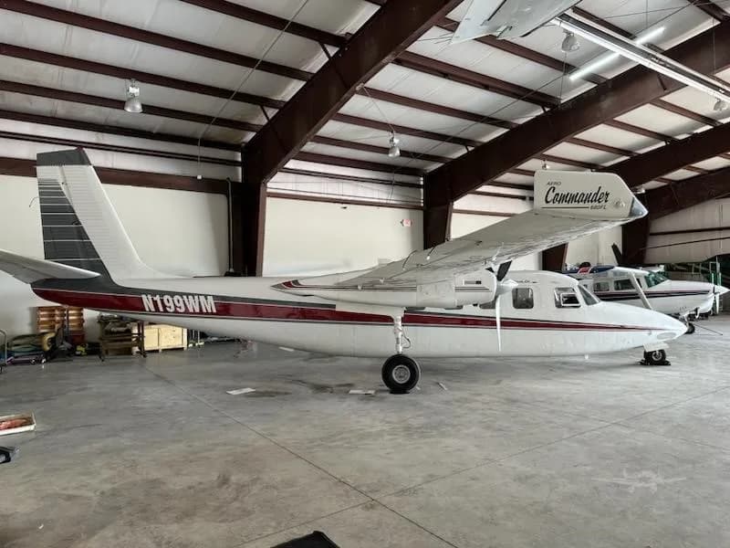 A side view of a white and red Aero Commander 680FL twin-engine aircraft, registration N199WM, parked in a hangar.