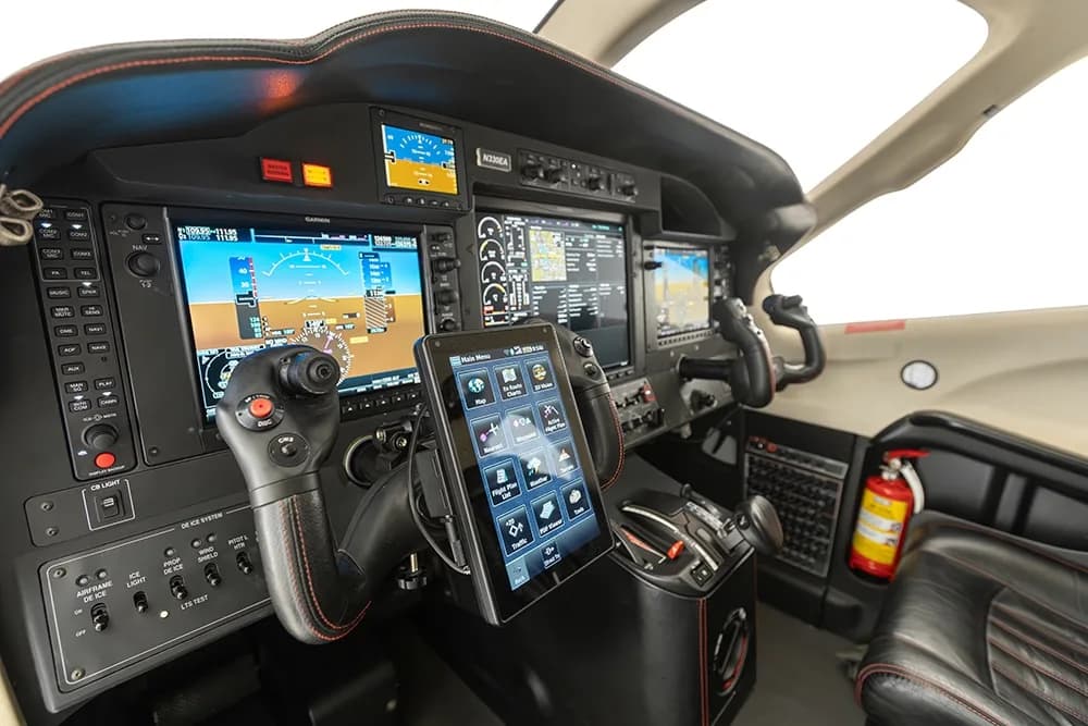 Angled view of the Daher TBM 900 cockpit, showing the pilot's side controls, instrument panel, and a fire extinguisher.