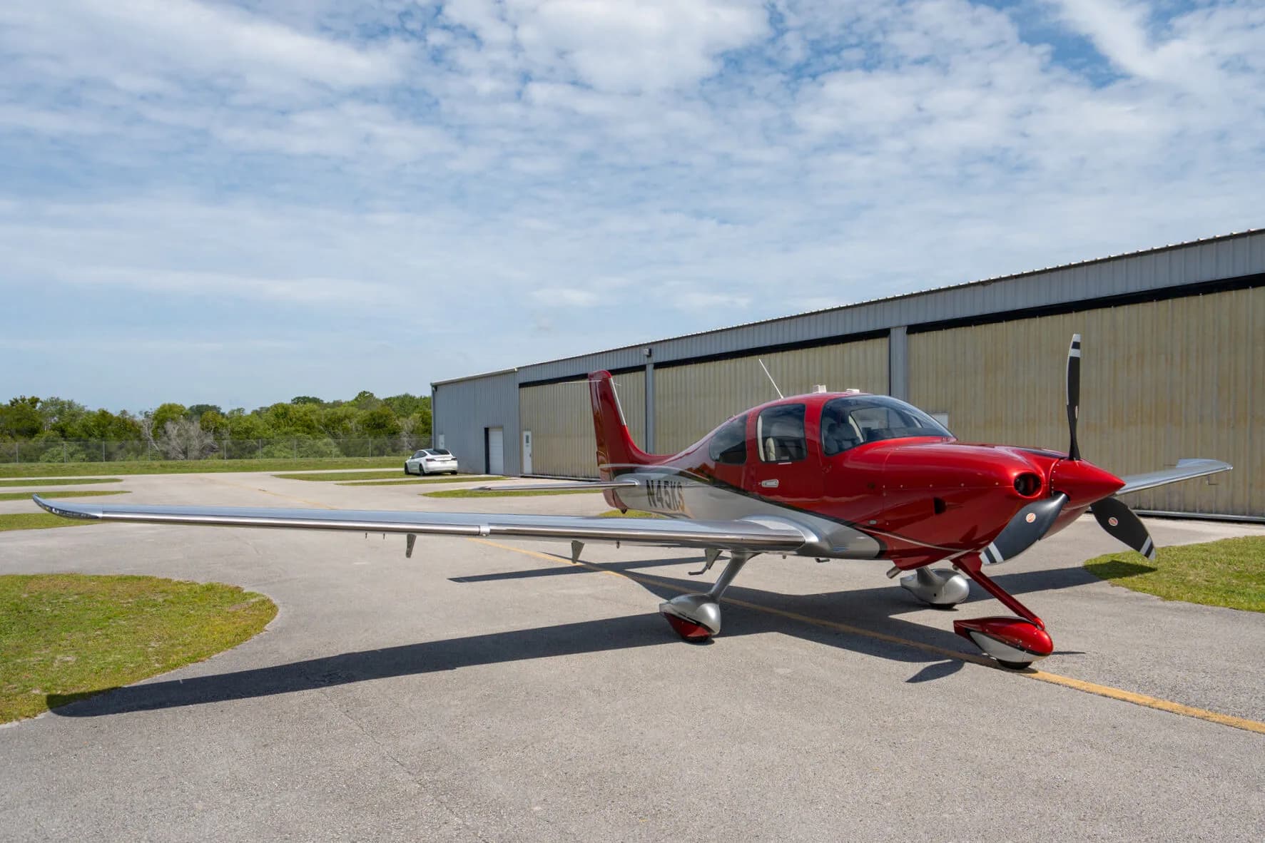 A red and silver Cirrus SR22 GTS (N45KS) parked on an airfield next to a hangar.