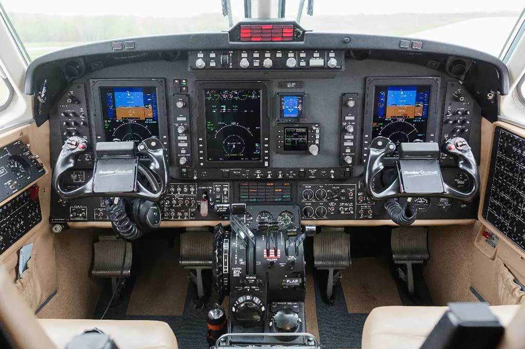The cockpit of a turboprop aircraft displays multiple digital screens, yokes, and control levers.