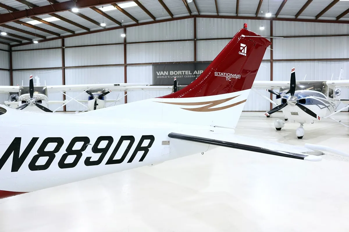 A close-up view of the tail section of a red and white Cessna Stationair TC aircraft (N889DR) with gold accents, parked in a hangar.