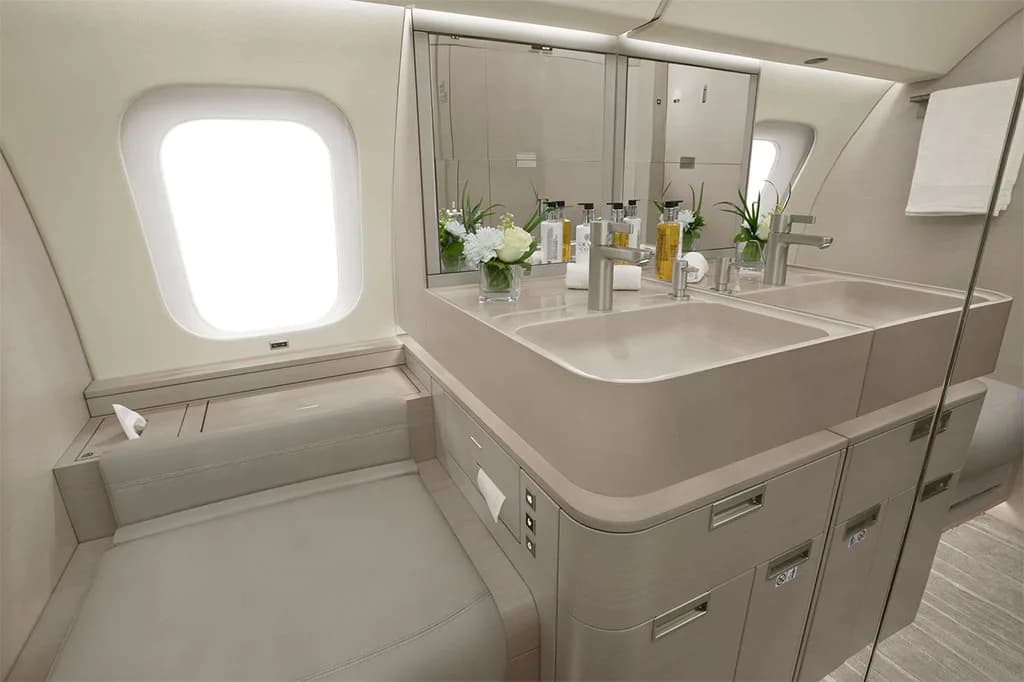 A luxurious aircraft lavatory with a double vanity, mirrors, and a window.