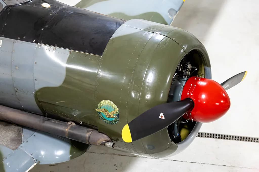 A close-up of the engine cowling and propeller of a vintage aircraft, featuring a red spinner and a 'Dependable Engines' logo.