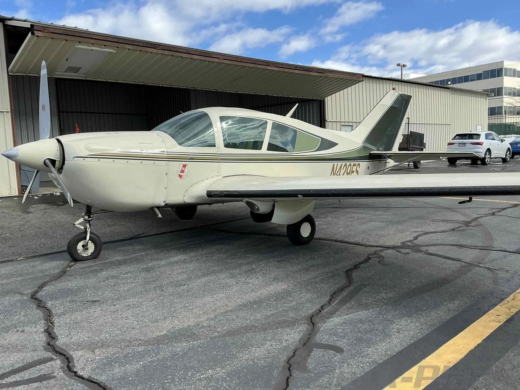 A front-quarter view of the white and green Bellanca Viking aircraft, N429FS, parked on an asphalt ramp near an open hangar.