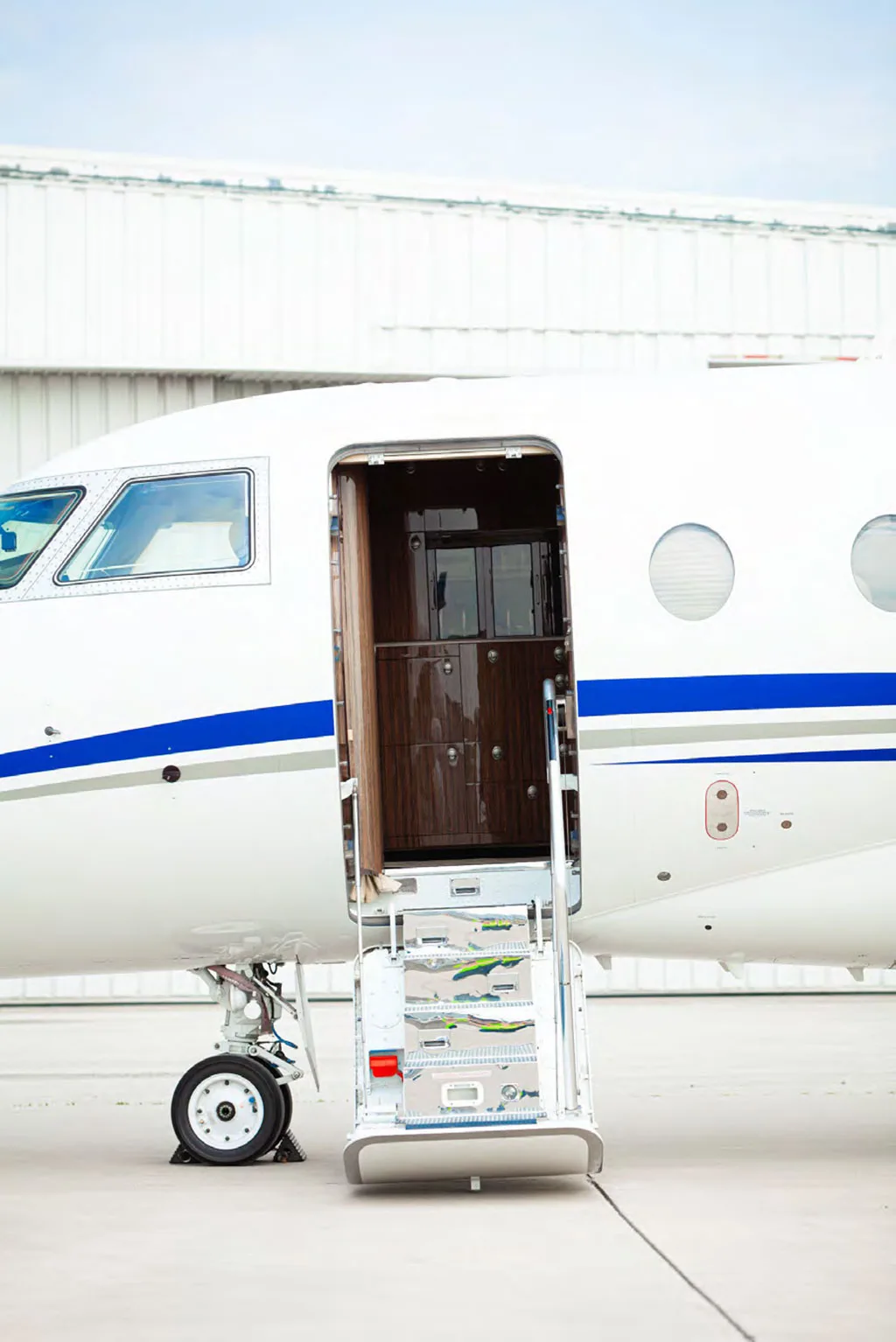 A close-up view of the white business jet's open main entry door with extended stairs, revealing a glimpse of the interior.