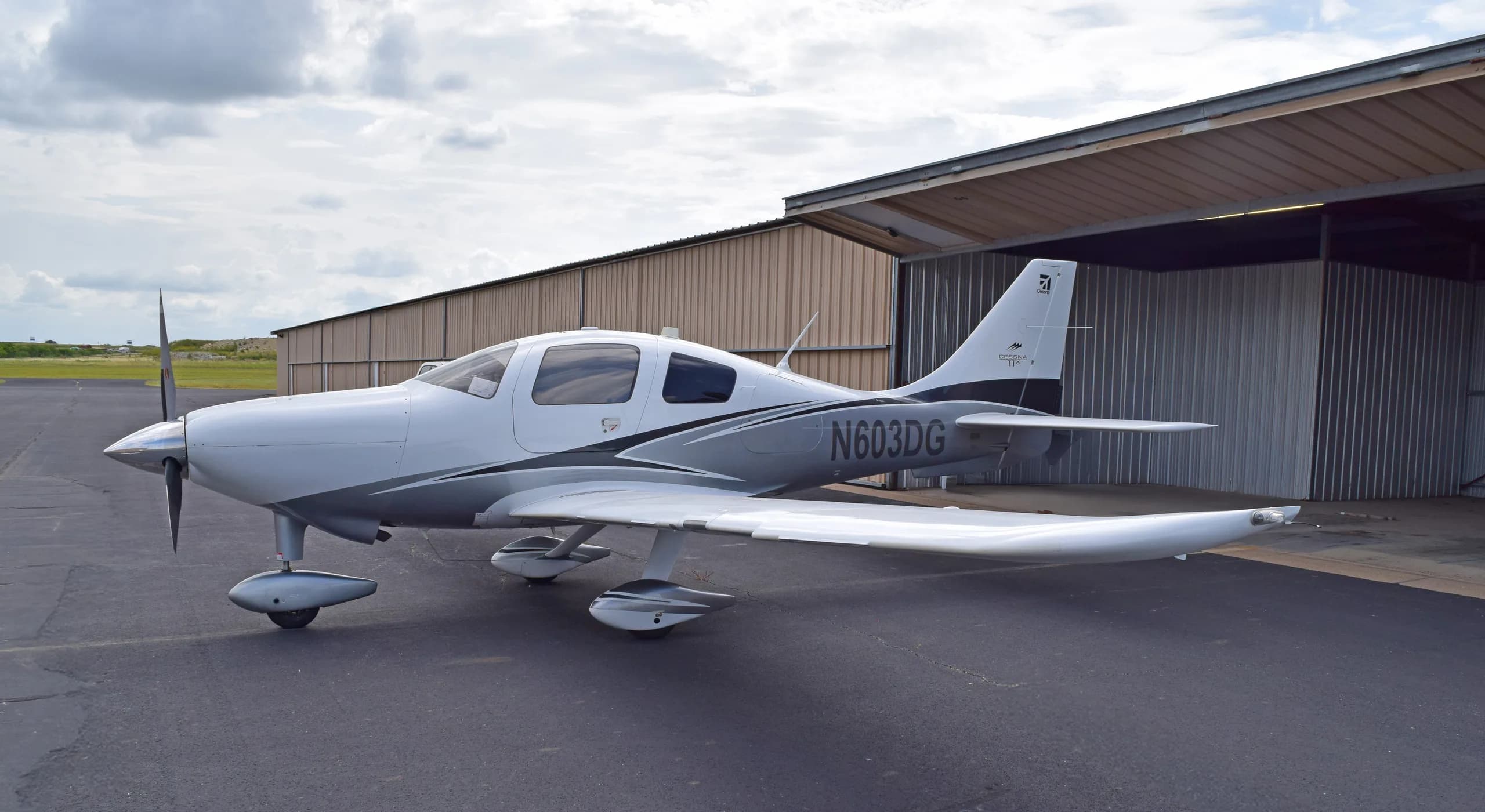 A white and grey Cessna TTx aircraft, N603DG, parked on an asphalt apron next to a hangar.