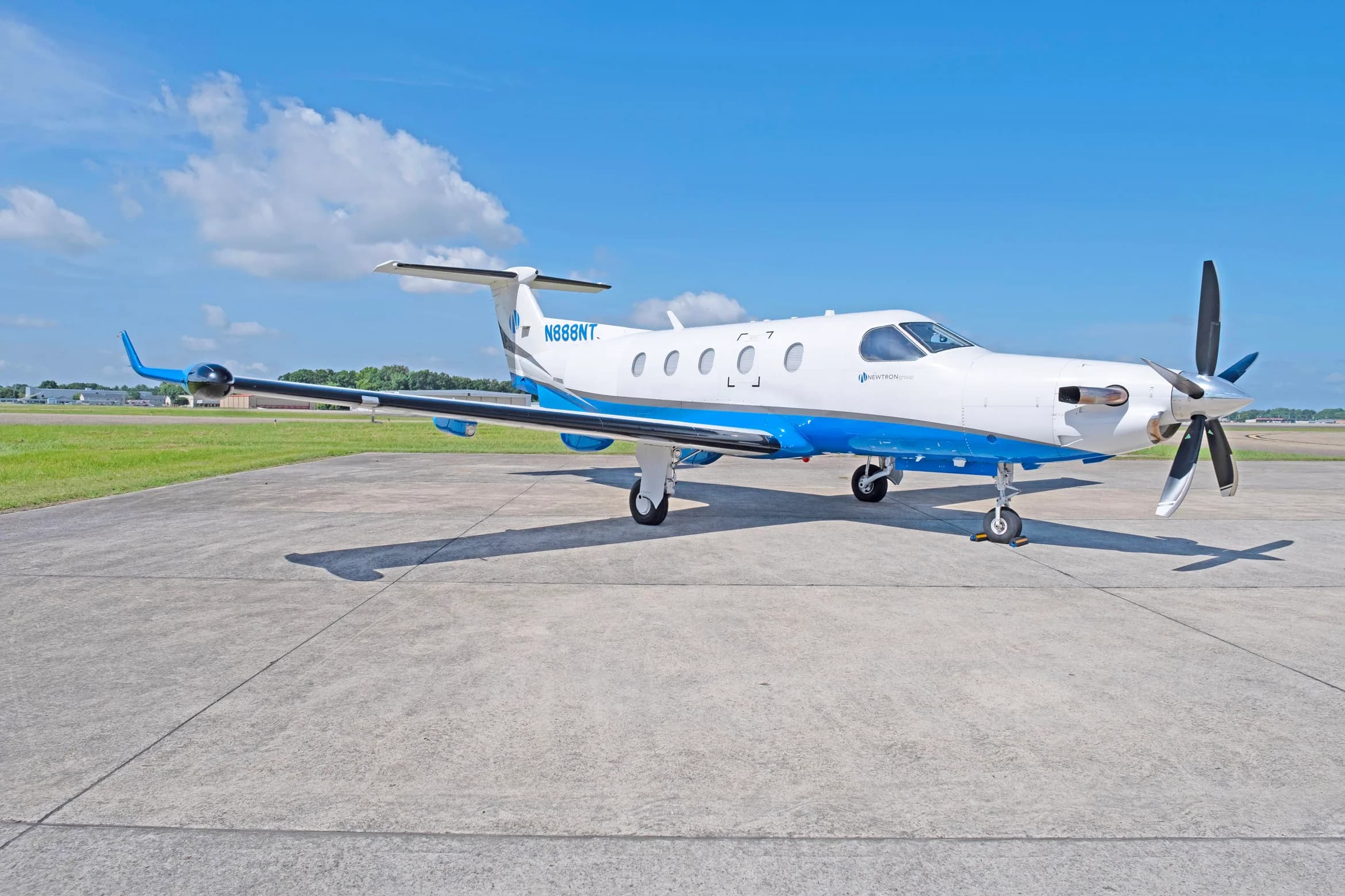 A white and blue Pilatus PC-12 aircraft, tail number N888NT, parked on a tarmac under a blue sky.