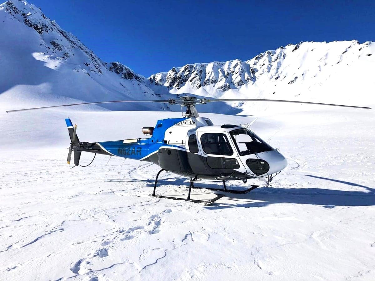 A blue and white helicopter parked on a snowy mountain landscape.
