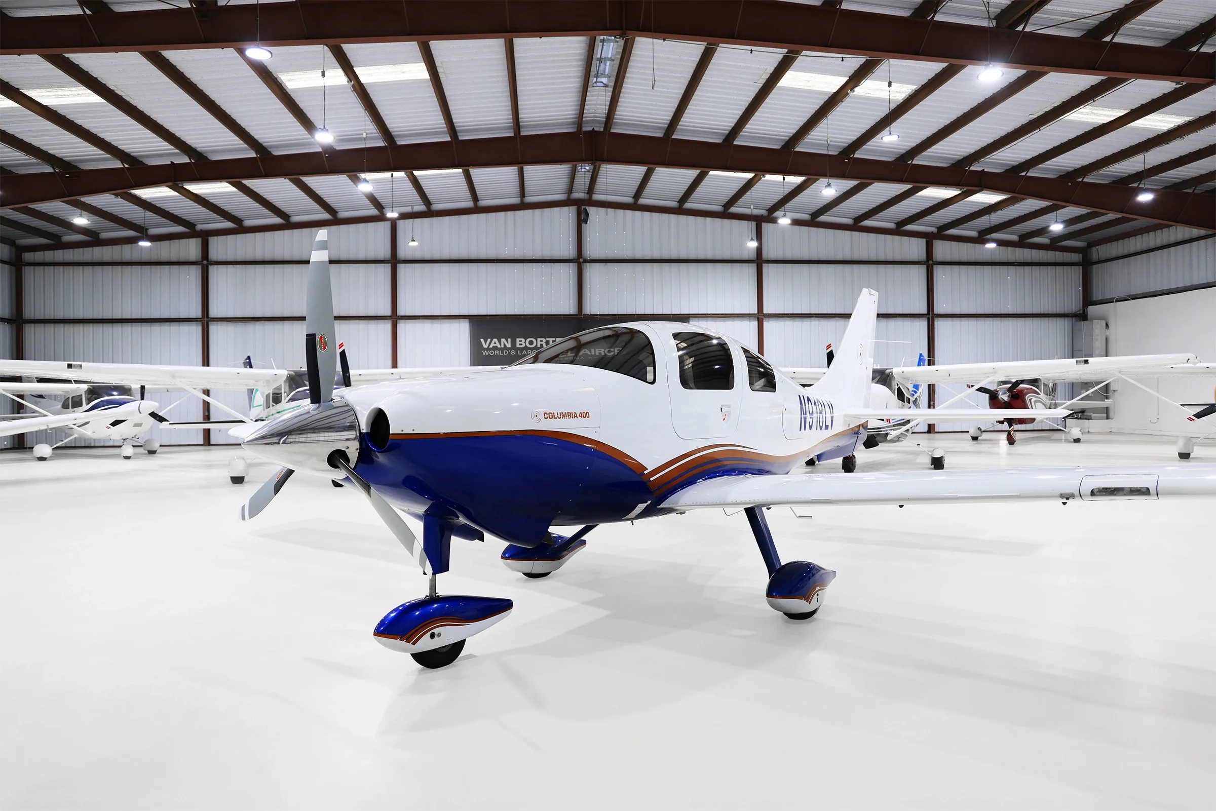 A white and blue Columbia 400 aircraft with registration N918LV is parked in a hangar, viewed from the front-right.
