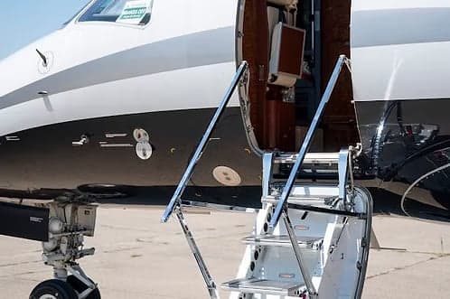A close-up view of the front fuselage and open boarding stairs of a private jet with a black and white paint scheme.