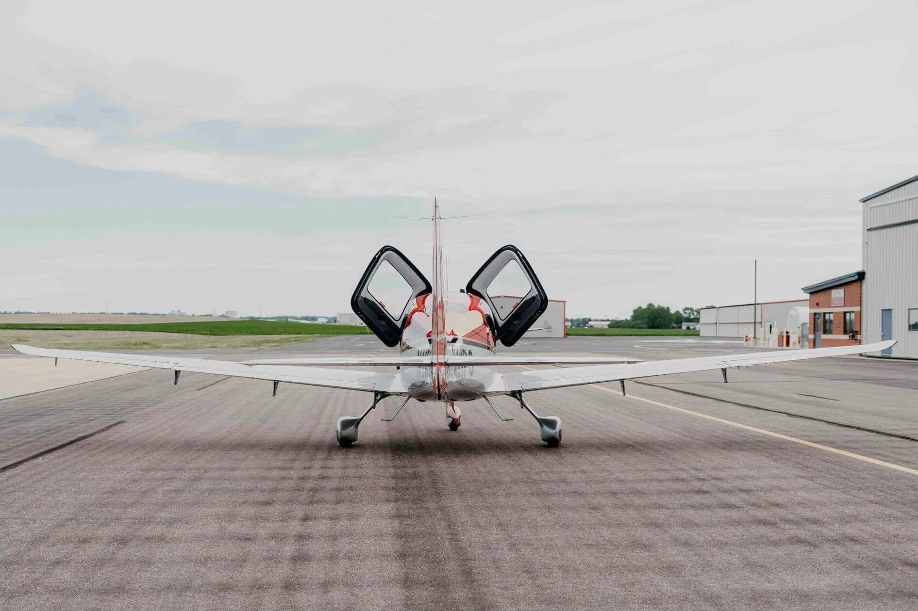 A rear view of the red and silver Cirrus SR20 Premium aircraft (N11PS) with both doors open, parked on the tarmac.