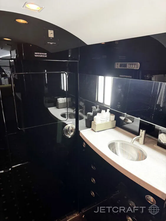 The private jet's lavatory with two stainless steel sinks, dark glossy walls, and various toiletries.