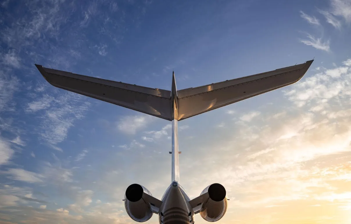 A low-angle view of the tail and two engines of a white business jet against a dramatic sunset sky.