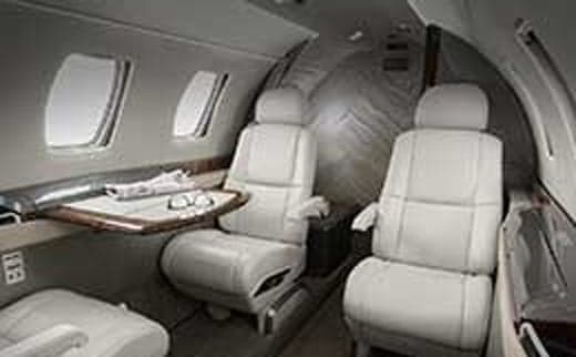 Interior of a jet with white leather seats and a small table.