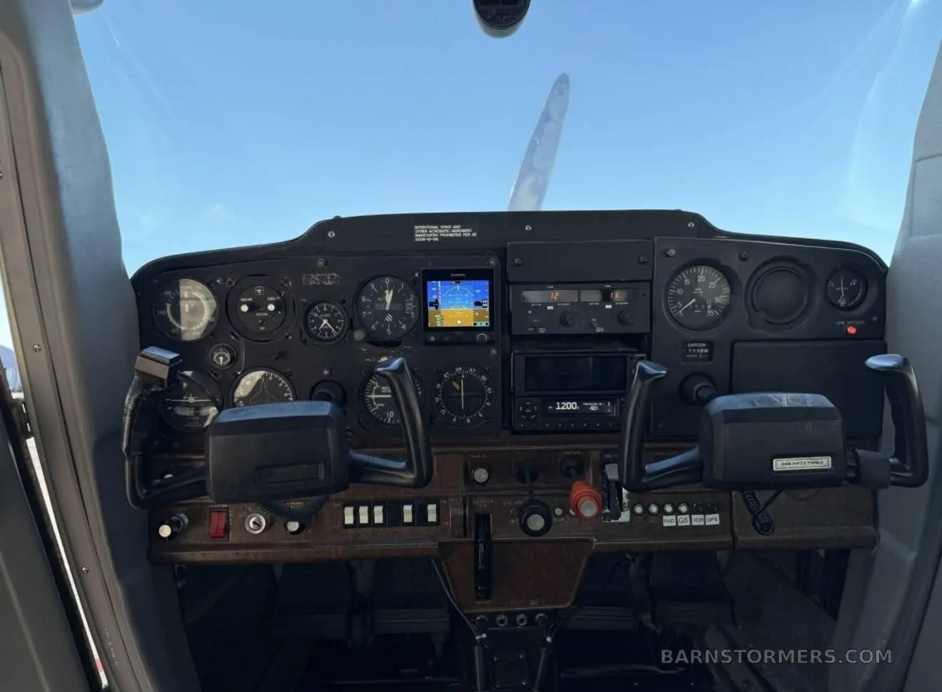 A full view of a small aircraft cockpit instrument panel with dual yokes and various gauges and screens.