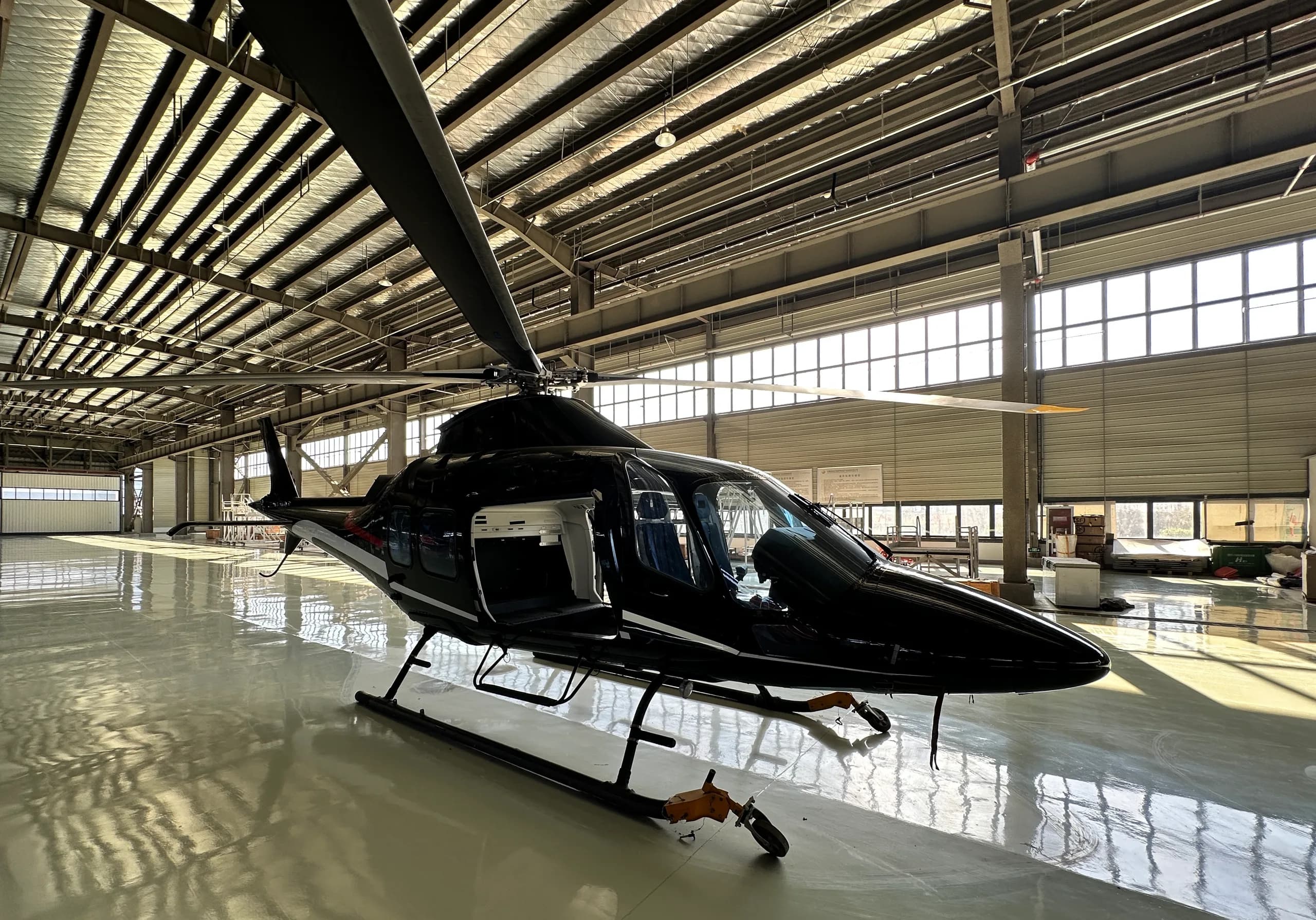 A sleek black helicopter with white and red accents is parked on a shiny floor in a brightly lit hangar, viewed from the front-right.
