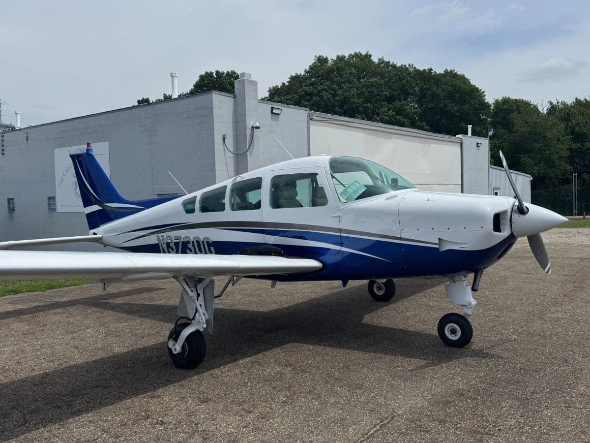 A white and blue single-engine aircraft, N3730G, parked on the tarmac with a building in the background.