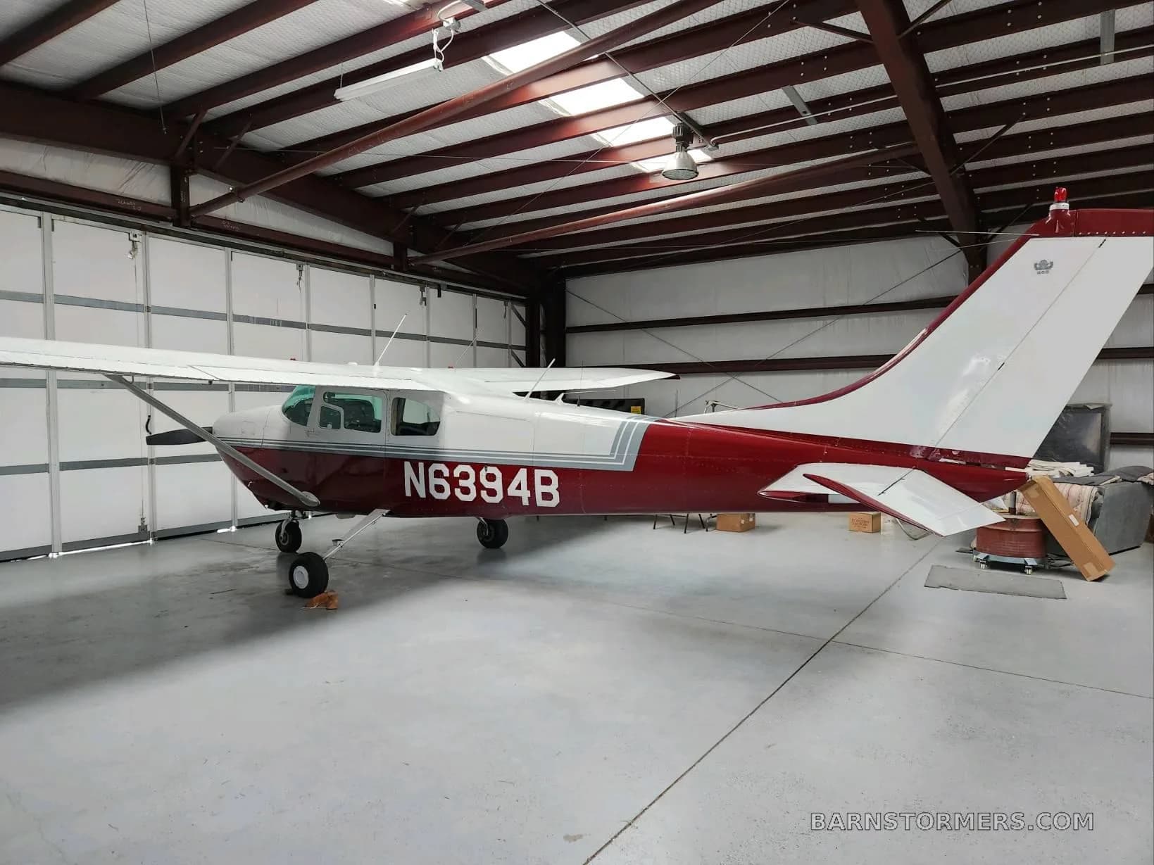 A red and white single-engine propeller aircraft (N6394B) parked inside a metal hangar.