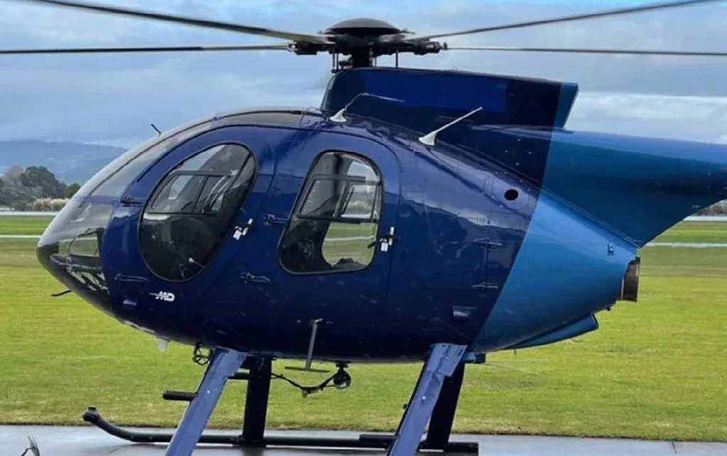 A close-up side view of the blue and light blue MD 530 helicopter on an airfield.