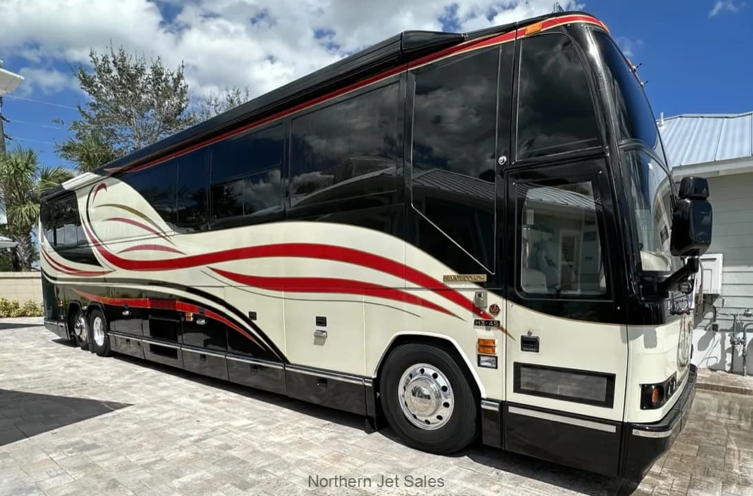 Front side view of a Prevost coach with a black, white, and red paint scheme parked outside.