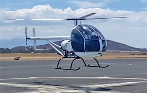 A white and blue helicopter takes off from a runway.