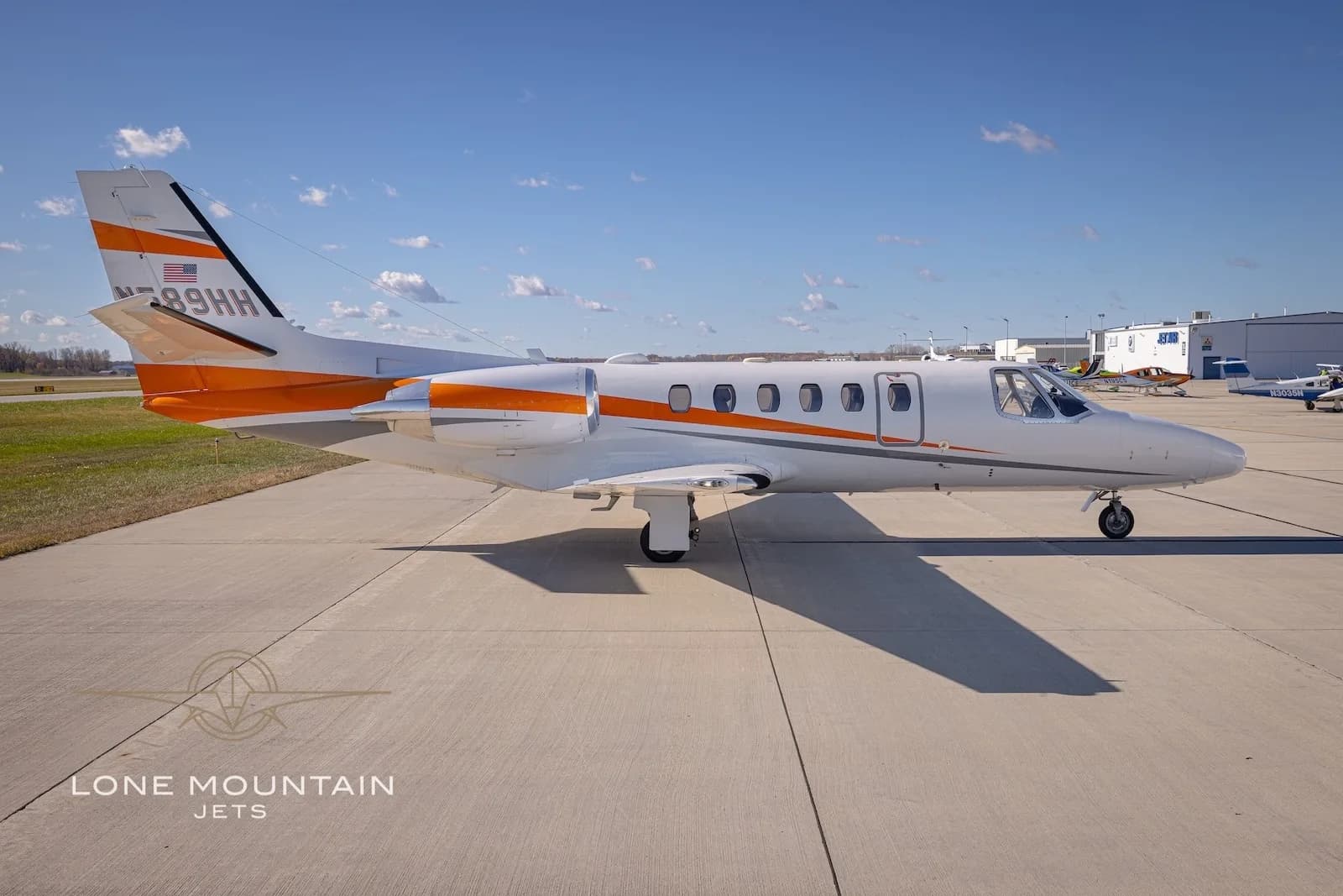 A side view of the white Cessna Citation Bravo business jet N589HH with orange and grey stripes on the tarmac.