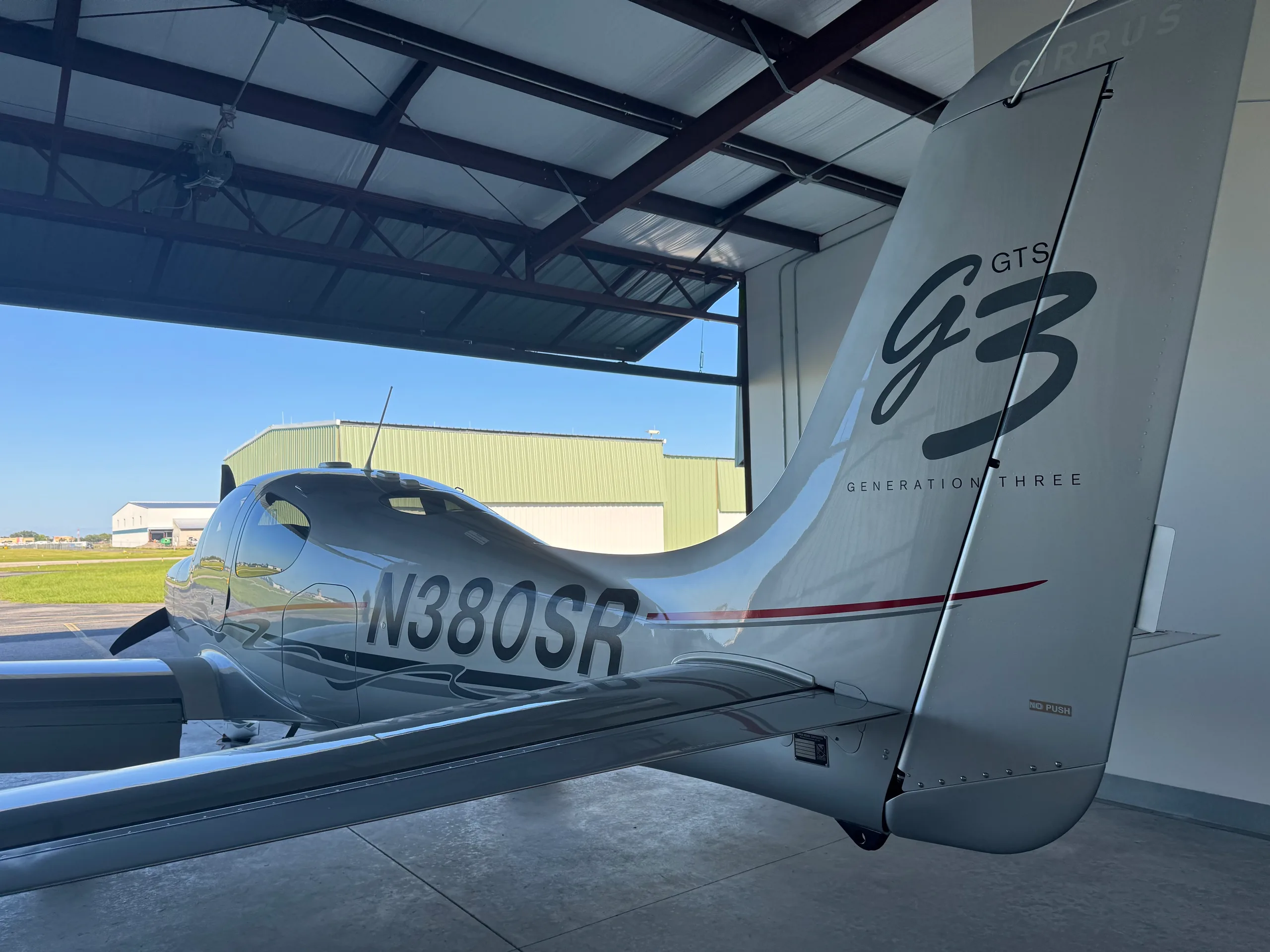 A silver Cirrus SR22 Generation Three aircraft with N380SR registration is parked in a hangar, viewed from the rear-left.