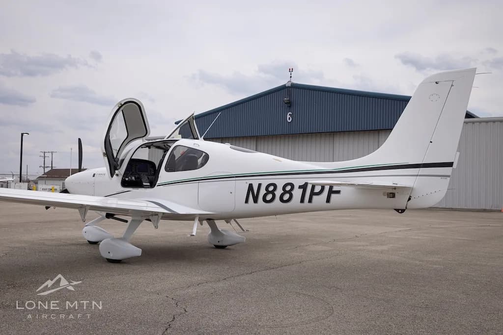 A rear-side view of a white Cirrus SR22 aircraft with N881PF registration and open doors, parked on an asphalt ramp.