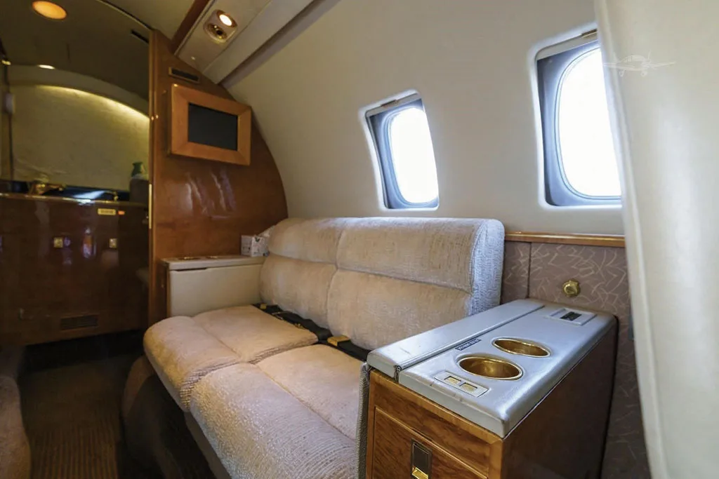 A comfortable beige fabric divan with an adjacent side table and cup holders in the aft section of the Dassault Falcon 50's cabin.