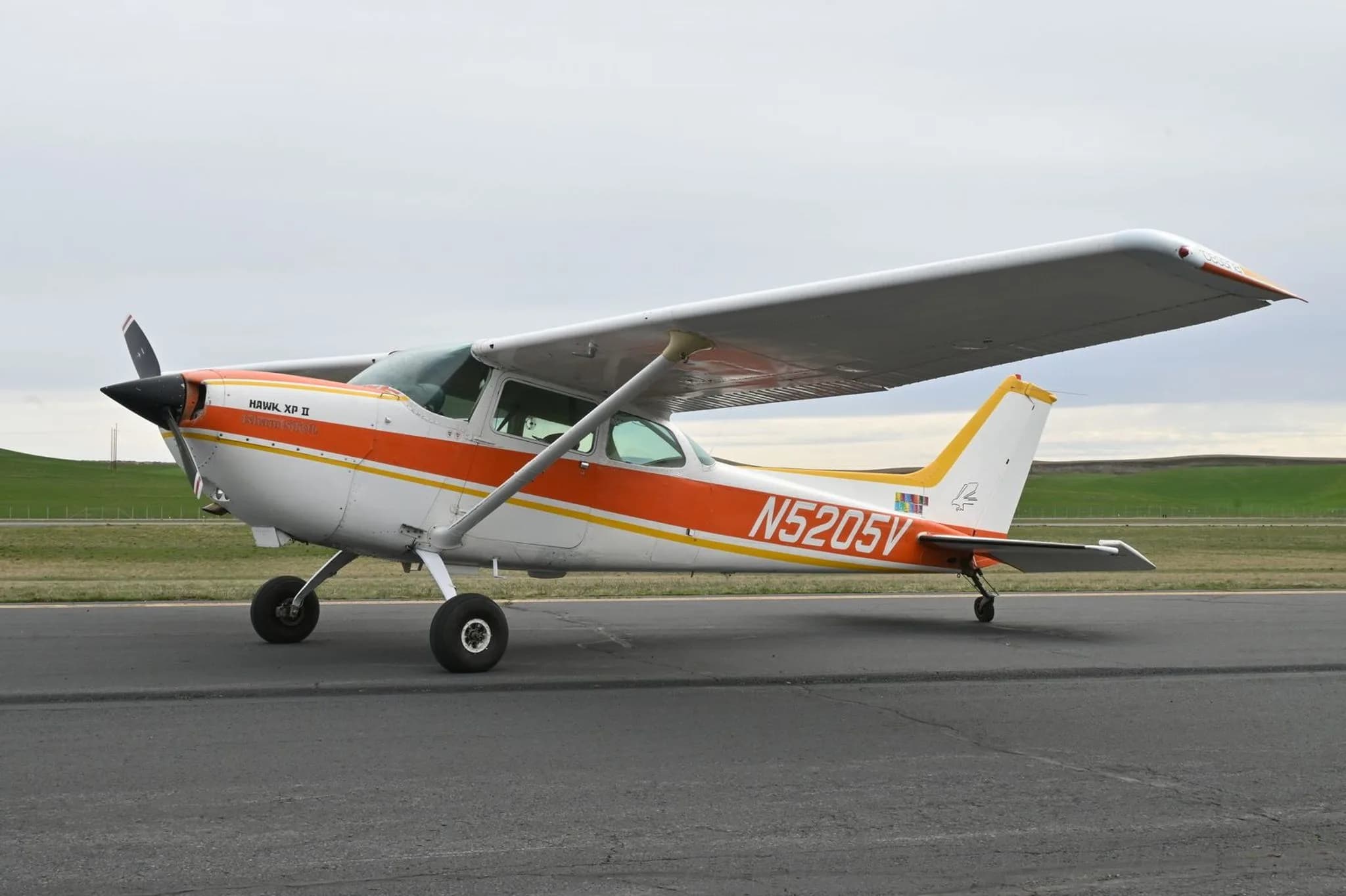A white and orange Cessna 172 Hawk XP II (N5205V) parked on an airfield, viewed from the front-left side.